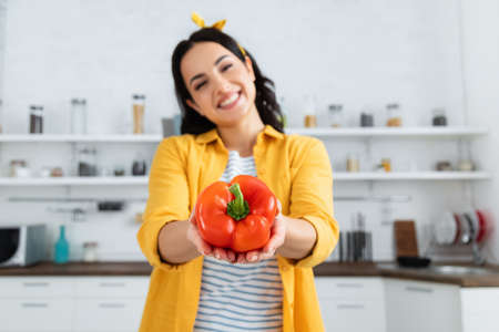 blurred and happy young woman holding red bell pepper