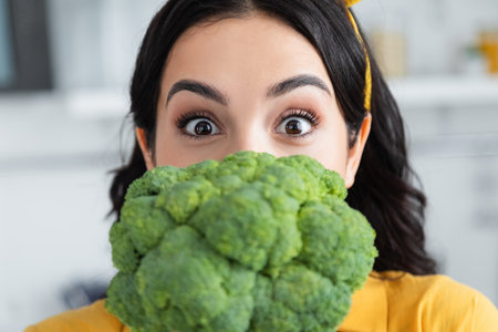 brunette woman looking at camera near ripe broccoliの写真素材