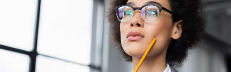 Low angle view of african american businesswoman with pencil looking away, bannerの写真素材