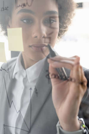 Blurred glass board near african american businesswoman with maker in officeの写真素材