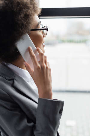 Smiling african american businesswoman in eyeglasses talking on smartphoneの写真素材