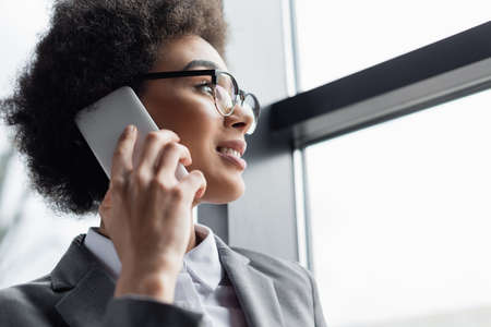 Low angle view of positive african american manager talking on smartphone near window
