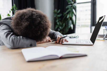 African american businesswoman lying on table near laptop and notebookの写真素材