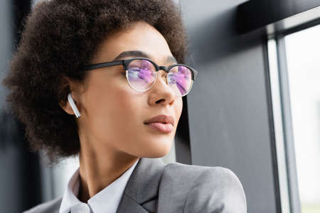 Young african american businesswoman in earphone standing near window in officeの写真素材