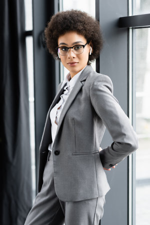 African american businesswoman in eyeglasses and earphones standing near windowの写真素材