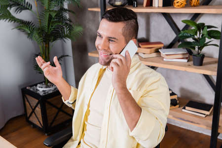 smiling man gesturing while talking on smartphone at home