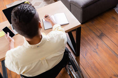 overhead view of disabled man writing in notebook while holding smartphone with blank screenの写真素材