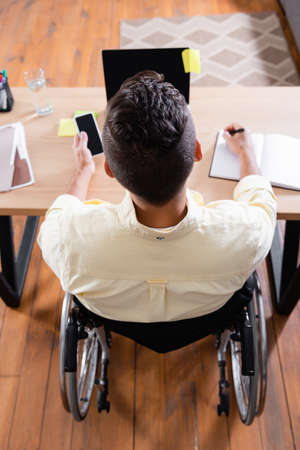 overhead view of disabled man writing in notebook while working near laptop at homeの写真素材