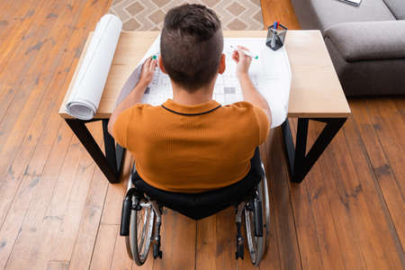 overhead view of disabled engineer working near blueprint at homeの写真素材