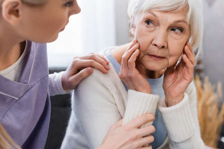 social worker touching shoulder of senior woman suffering from amnesia, blurred foreground