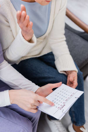 cropped view of social worker pointing at calendar near senior woman suffering from memory lossの写真素材