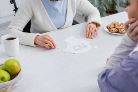cropped view of elderly woman and nurse playing jigsaw puzzle at homeの写真素材