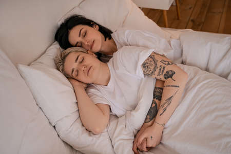 high angle view of young lesbian couple lying in bed and holding handsの写真素材