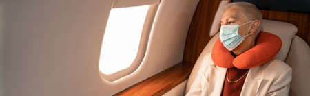 Mature businesswoman in neck pillow and medical mask in plane, banner