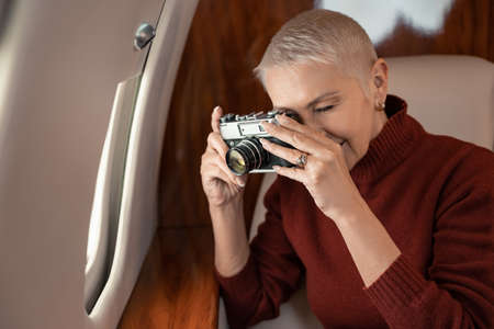 Mature woman taking photo on retro camera near window of plane