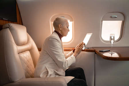 Side view of mature businesswoman using digital tablet near smartphone and glass of champagne in...