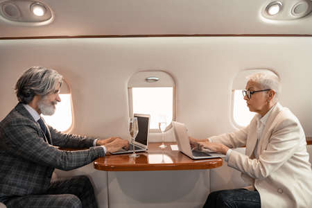 Side view of business people using laptops near champagne in private jet