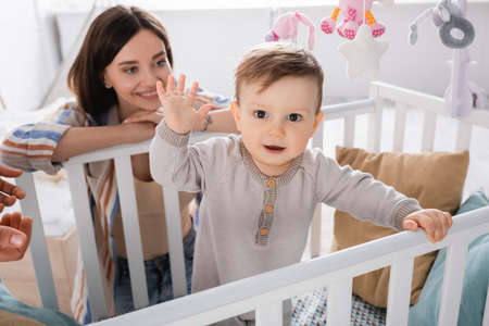 infant boy waving hands near happy tattooed mother on blurred background