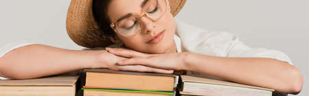 young woman in straw hat and glasses leaning on pile of books isolated on white, banner