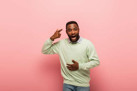Excited african american man pointing at head on pink background