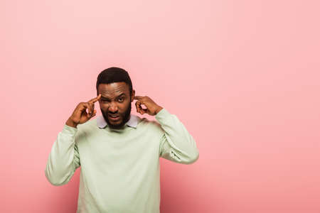 Confused african american man pointing at head on pink background