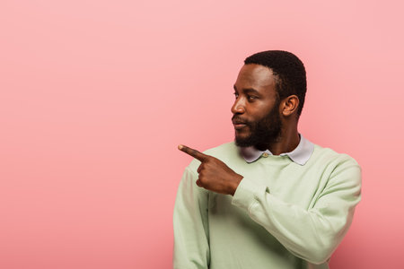 African american man in jumper pointing away with finger isolated on pinkの写真素材
