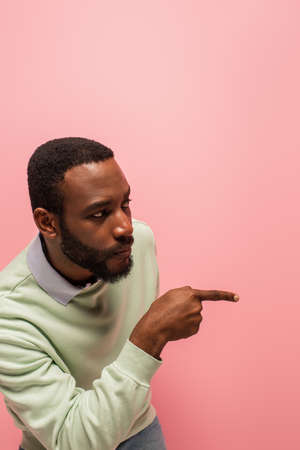 African american man in jumper pointing with finger away isolated on pinkの写真素材