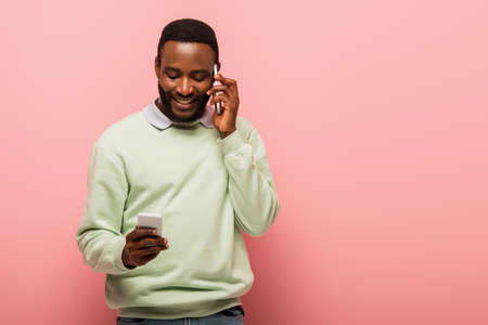 Young african american man talking and using cellphone on pink backgroundの写真素材