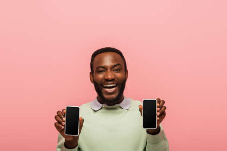 Cheerful african american man with cellphones isolated on pinkの写真素材