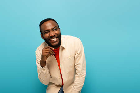 cunning african american man smiling while looking away isolated on blueの写真素材