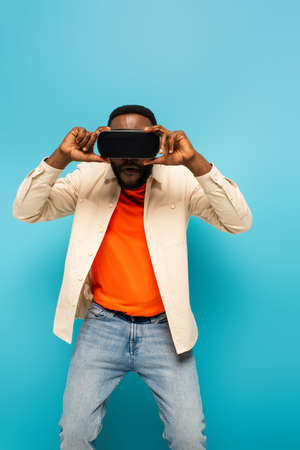 african american man adjusting vr headset on blue backgroundの写真素材