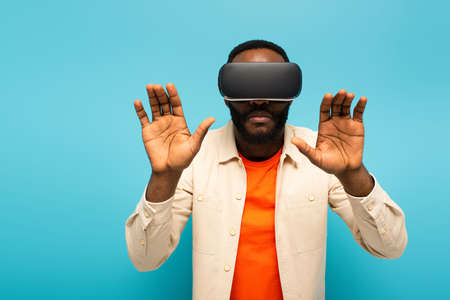 african american man in vr headset touching something isolated on blueの写真素材