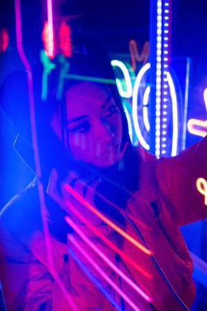 neon lighting near young asian woman talking on retro payphone outsideの写真素材