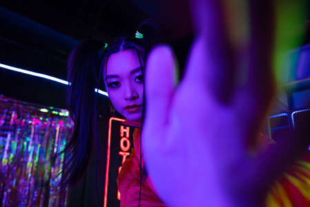 young asian woman with blurred hand near neon sign with hotel lettering outside