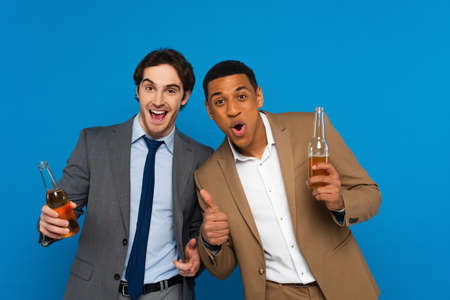 interracial friends in suits celebrating success with beer bottles and thumbs up gestures isolated...