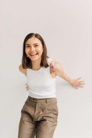 laughing young woman in white top and beige trousers on gray backgroundの写真素材