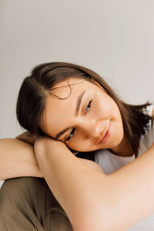 thoughtful young woman with perfect skin sitting with head putted on crossed arms on gray background