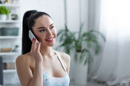 pretty woman in sportswear looking away while talking on cellphone at homeの写真素材