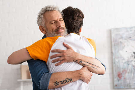 Young man hugging mature father at homeの写真素材