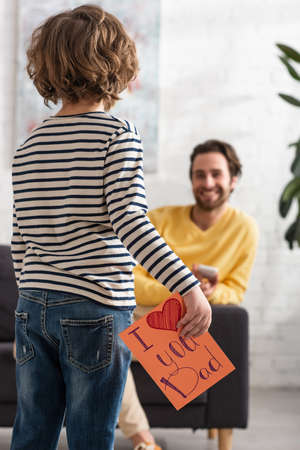 Boy holding gift card with i love you dad lettering near blurred fatherの写真素材
