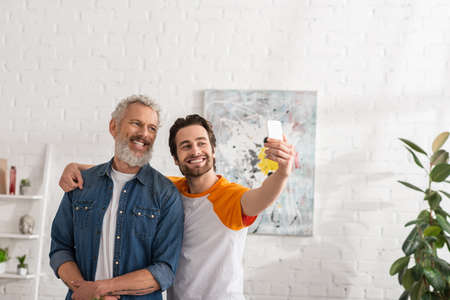 Son hugging father and taking selfie with smartphone in living roomの写真素材