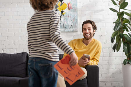Smiling man with smartphone looking at son with gift cardの写真素材
