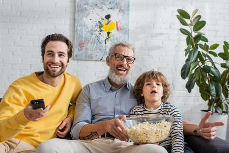 Smiling men and boy watching tv with popcorn at home
