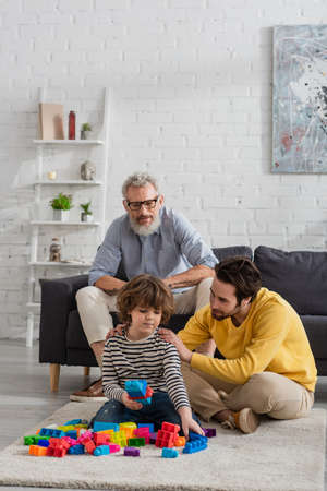 Man hugging son with building blocks near grandfather on couchの写真素材