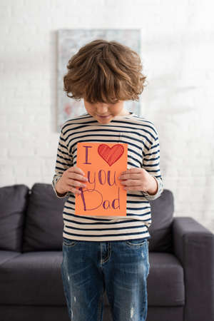 Boy looking at gift card with i love you dad lettering at homeの写真素材