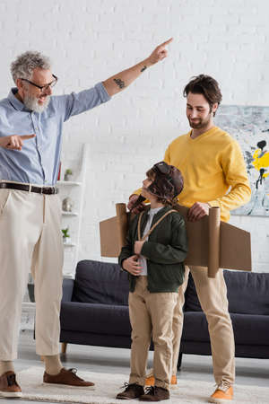 Cheerful grandfather pointing with fingers near boy in aviator costume and sonの写真素材