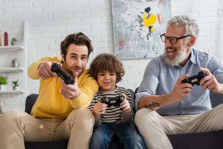 KYIV, UKRAINE - APRIL 12, 2021: Young man playing video game with son and father on couch