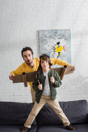 Excited father and kid in aviator helmet and wings looking at camera