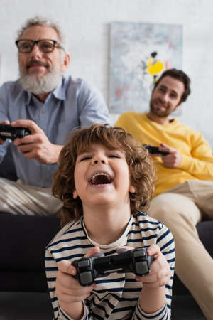 KYIV, UKRAINE - APRIL 12, 2021: Excited kid playing video game near blurred parents