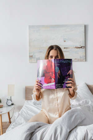 Woman covering face with magazine on bedの写真素材